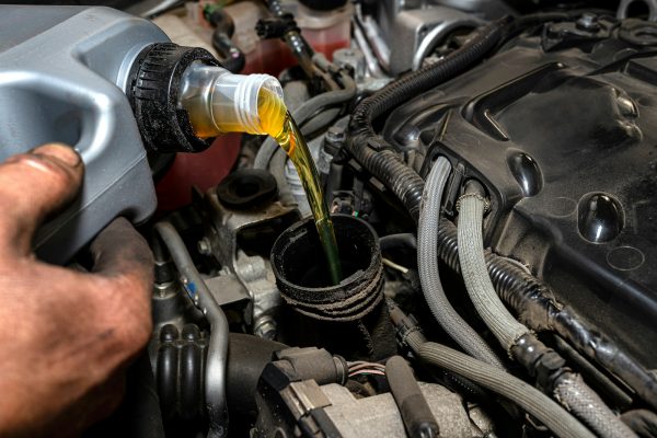 Car mechanic pours new car oil into the engine from a plastic tank in a car workshop.